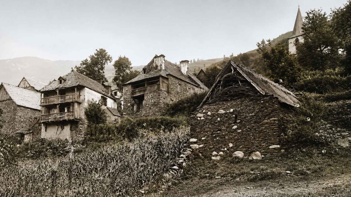 Vista històrica de Bausen a començaments del segle XX, amb cases de pedra, bordes, camps de cultiu i l’església de Sant Pèir dominant el poble.