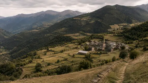 Paisatge de la Vall d’Àssua, amb un poble envoltat de prats, boscos i muntanyes del Pirineu.