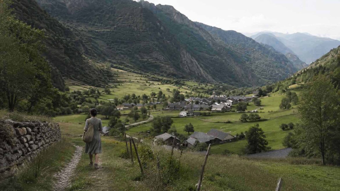 Dona caminant per un antic camí en direcció a Àreu, a la Vall Ferrera, amb el poble, els camps i els vessants muntanyosos de la vall al fons. Porta un vestit d’estil anys trenta i una bossa amb les seves pertinences.