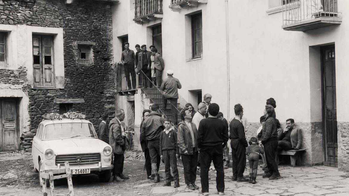 Grup d’excursionistes i habitants reunits davant de la fonda de Bonaventura Jubany, al poble d’Àreu, a la Vall Ferrera, l’any 1963. A l’esquerra, un automòbil carregat d’equipatge testimonia l’arribada dels visitants per carretera.