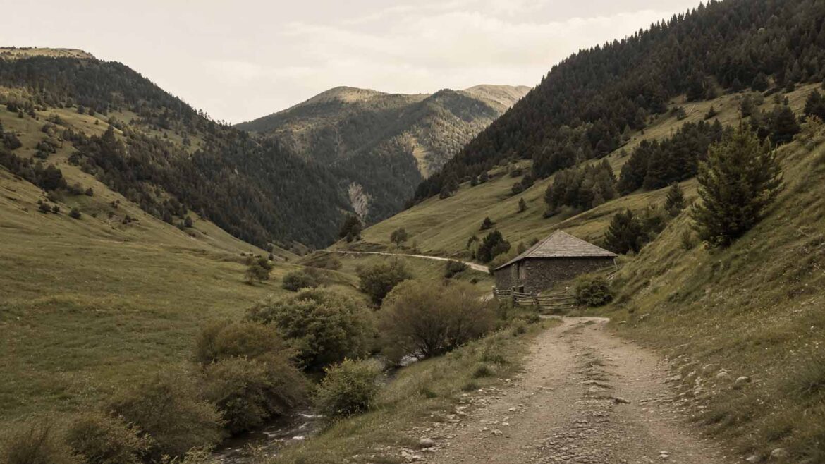 Paisatge del port de Cabús, amb un camí de muntanya que travessa les pastures entre vessants coberts de boscos. Al costat del camí hi ha una construcció tradicional de pedra i, al fons, s’estenen les muntanyes que separen la Vall Ferrera d’Andorra.