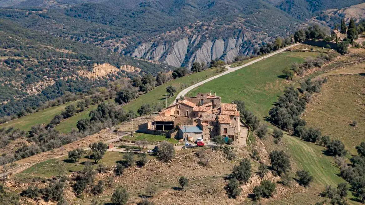 Vista panoràmica de Vilamolat de Mur, al Pallars Jussà, amb les cases de pedra agrupades entre camps i relleus de muntanya.