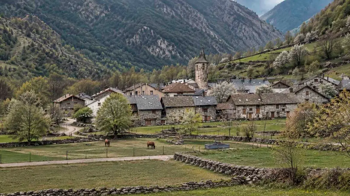 Vista general d’un poble pirinenc envoltat de prats, horts, murs de pedra i vessants de muntanya, que mostra la relació entre les cases i el territori que les envolta.