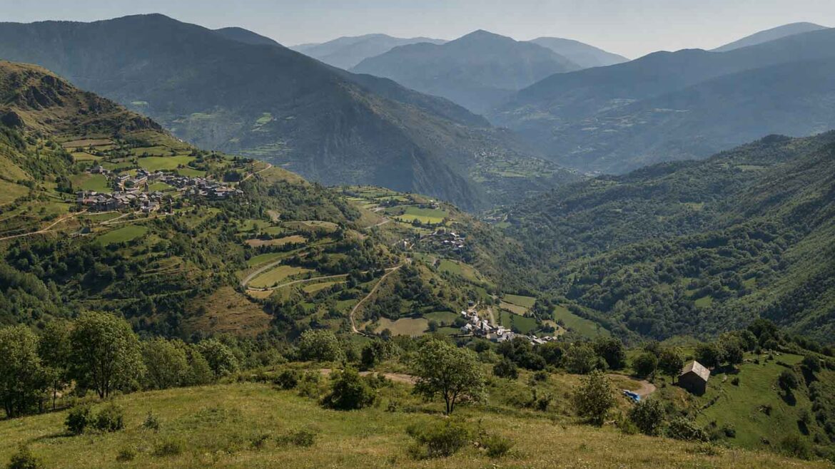 Vista panoràmica de la Vall d’Àssua, al Pallars Sobirà, amb petits nuclis habitats, prats i boscos distribuïts pels vessants i les muntanyes al fons.