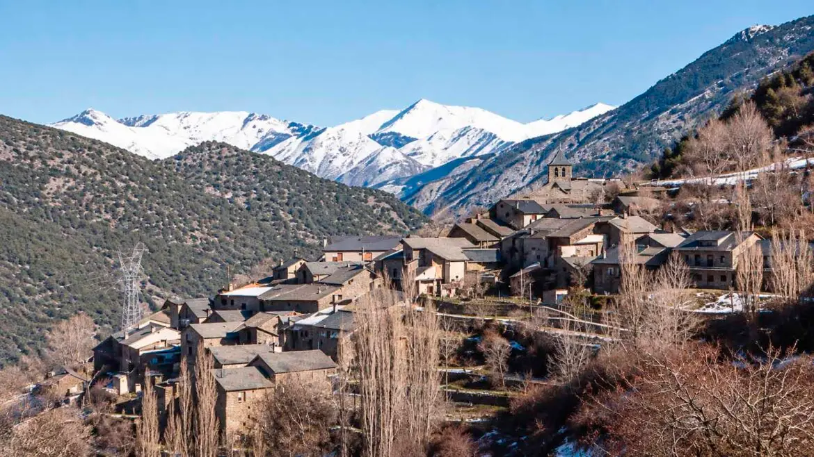 Vista del poble de Roní, al Pallars Sobirà, amb les cases agrupades al vessant i les muntanyes nevades al fons.